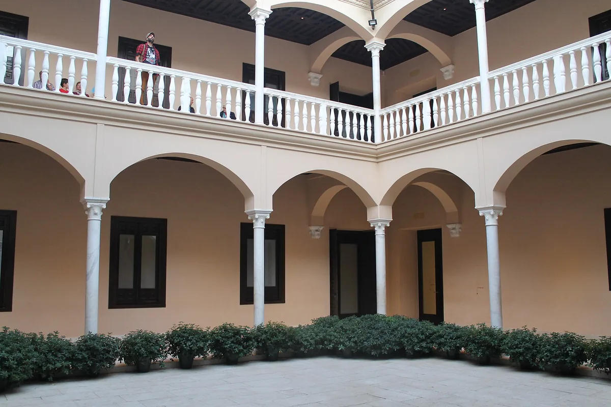 The courtyard of the Museo Picasso Málaga, with pale arched galleries around a paved patio and an old tree